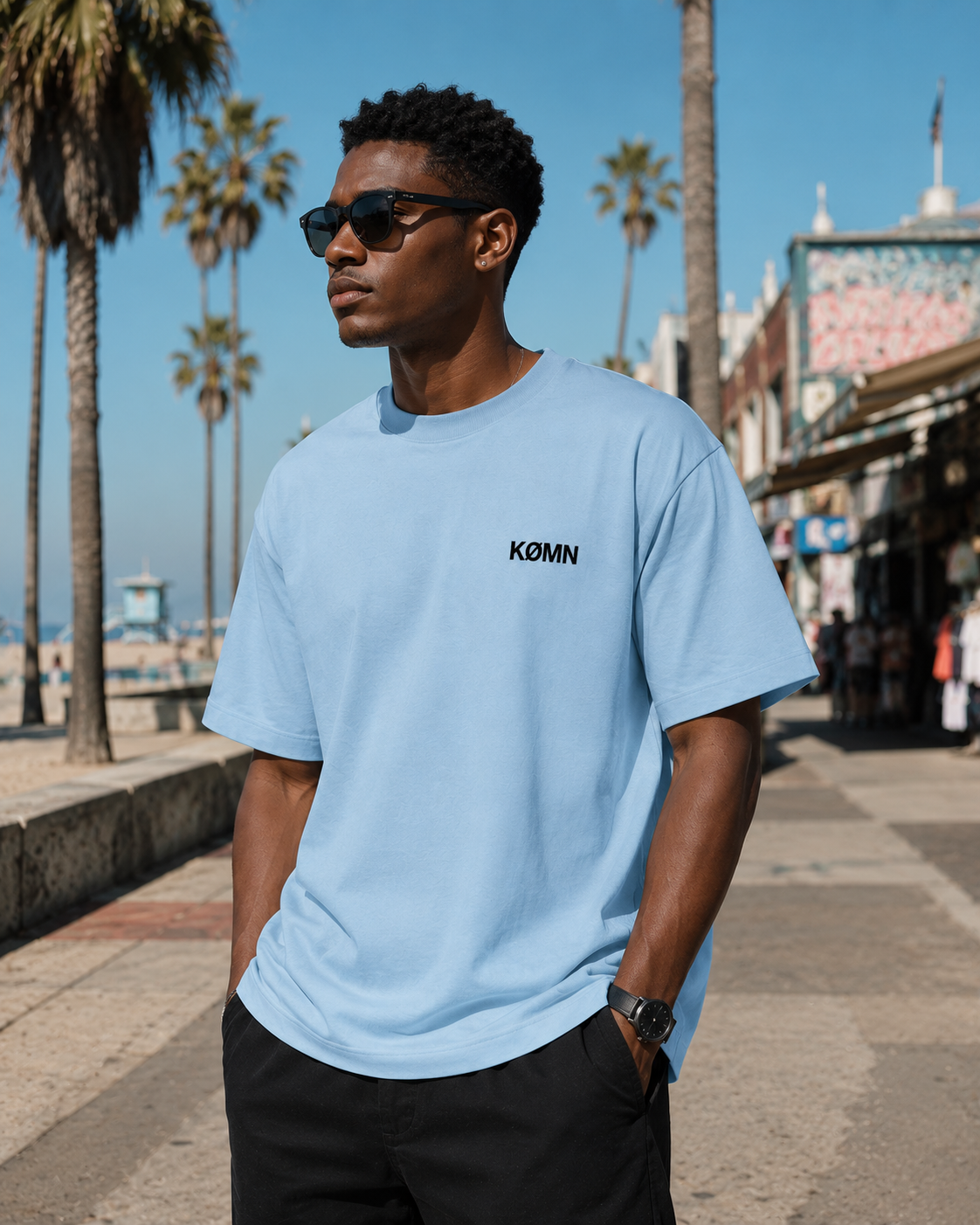 Men wearing KØMN sky blue oversized t-shirt with black chest logo front view, 200 GSM cotton crewneck tee