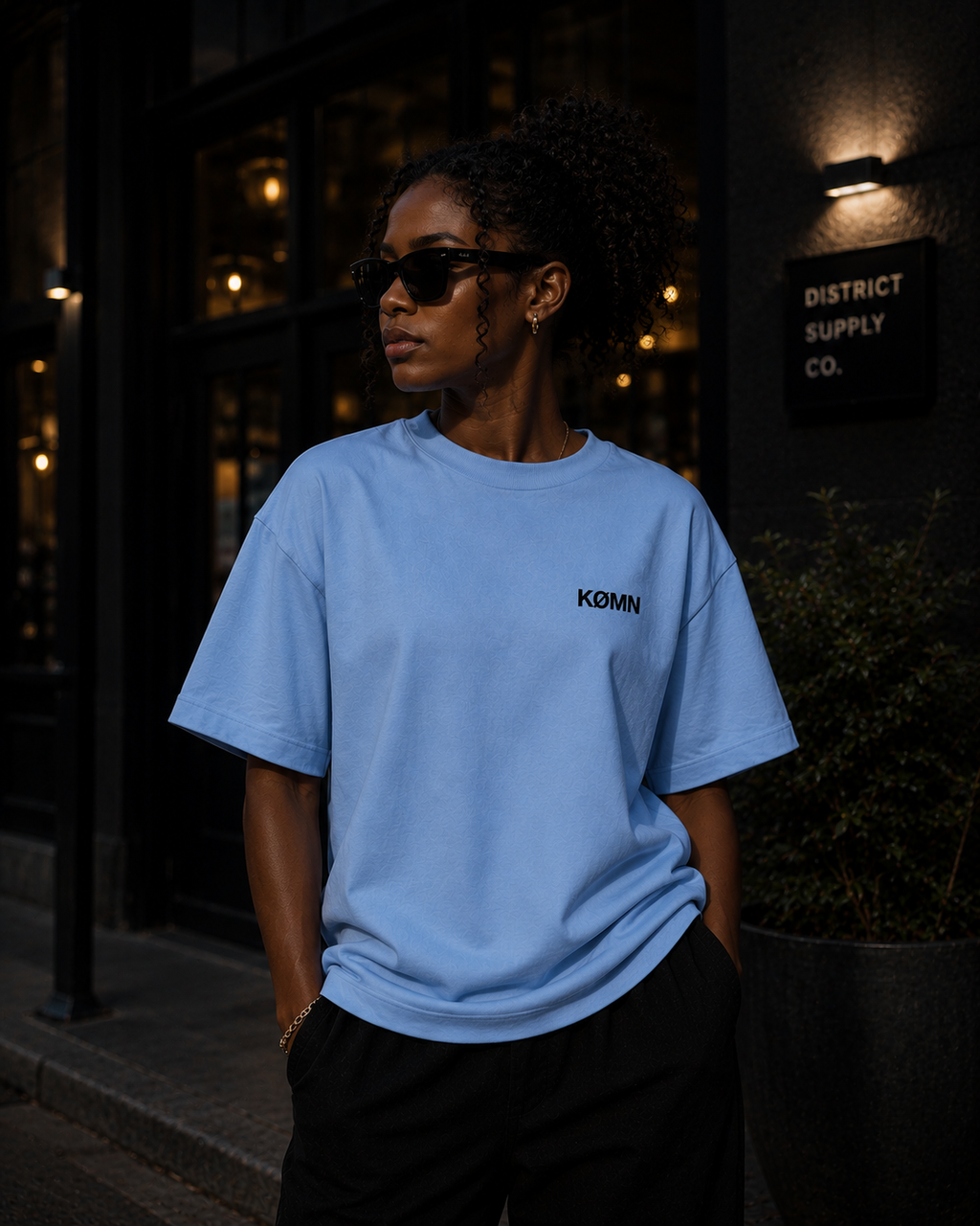 Woman wearing KØMN light blue oversized t-shirt with black chest logo, minimal cotton oversized tee