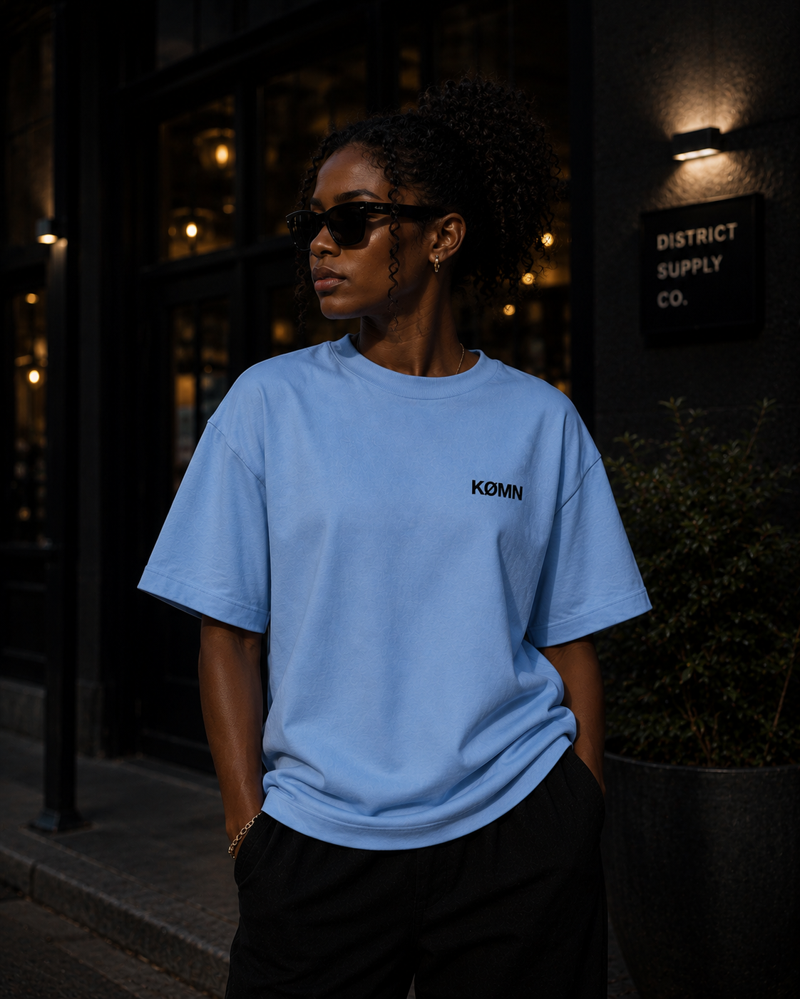 Woman wearing KØMN light blue oversized t-shirt with black chest logo, minimal cotton oversized tee