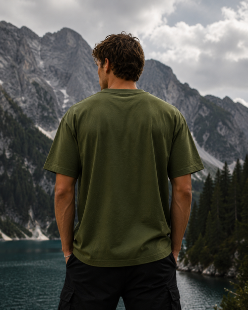 Back view of man in KØMN olive green oversized cotton t-shirt, relaxed fit casual outdoor streetwear look